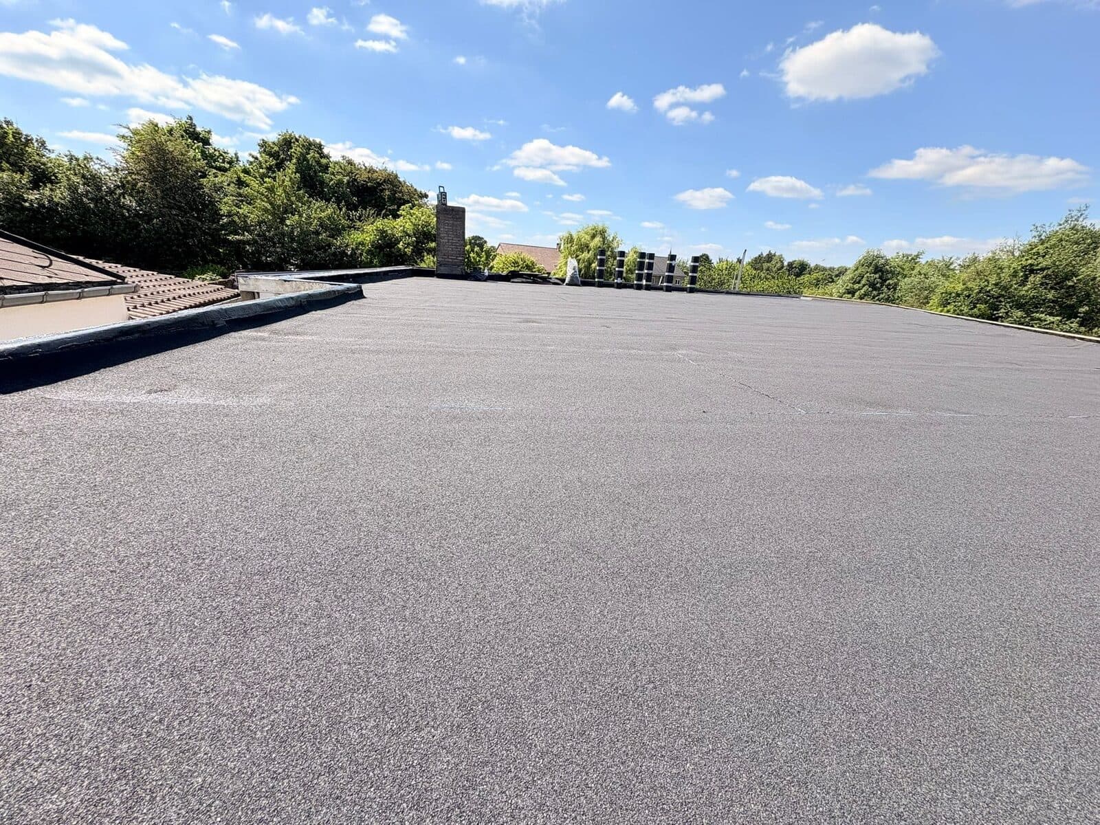 Toiture plate étanchée en roofing bitumineux, avec relevés en périphérie et souche de cheminée traitée